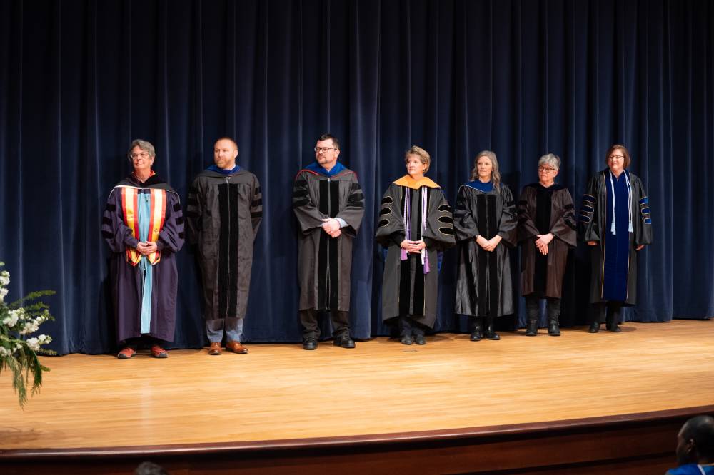 7 faculty stand on stage waiting to accept their award.